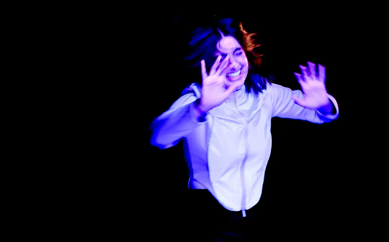 Tanvi Virmani mid-movement, lit in violet against black, for Nottingham Theatres